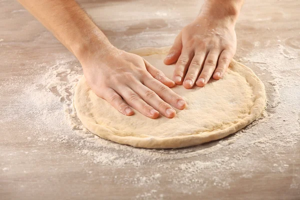 Mãos preparando base de massa para pizza na mesa de madeira, close-up — Fotografia de Stock