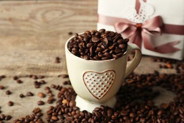 Bonito presente com arco e grãos de café na caneca, no fundo de madeira — Fotografia de Stock