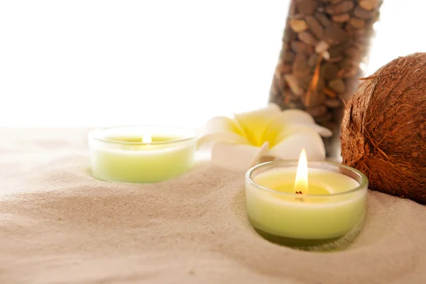Plumeria s hořící svíčky, kokos a láhev na písku, izolovaných na bílém — Stock fotografie