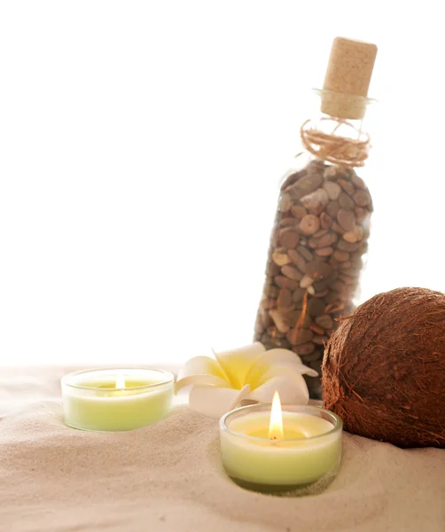 Plumeria mit brennenden Kerzen, Kokosnuss und Flasche auf Sand, isoliert auf Weiß — Stockfoto
