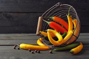 Chili peppers in basket, on wooden background
