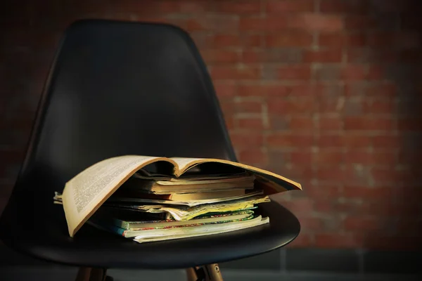 Pile of old books on black chair against brick wall, close up — Stock Photo, Image