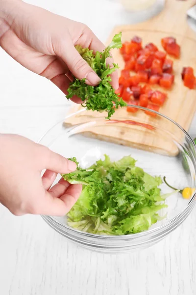 Руки женщины добавляют листья салата в миску с салатом, крупным планом — стоковое фото