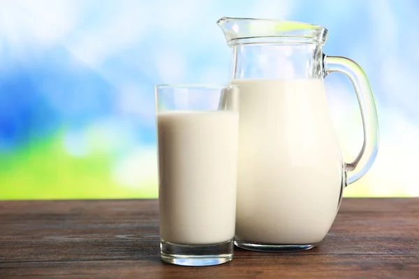 Melk in pot en in glas op tafel op wazig natuurlijke achtergrond — Stockfoto