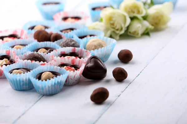 Conjunto de doces de chocolate com flores em um fundo de madeira leve, close-up — Fotografia de Stock