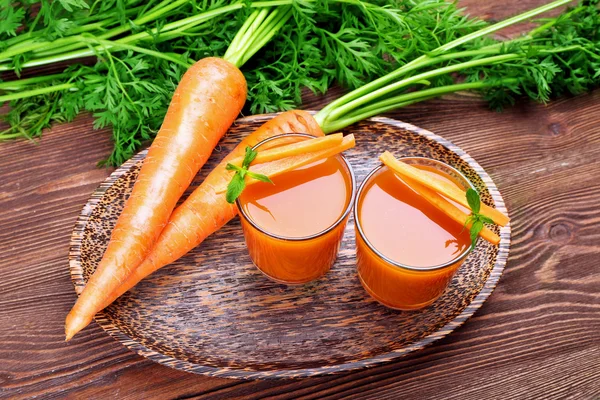 Se acercan los vasos del jugo de zanahoria con hortalizas a la mesa —  Fotos de Stock