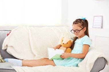 Kitap ile kanepede oturan küçük kız 