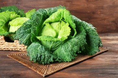 Savoy cabbage in wicker basket on wooden background clipart