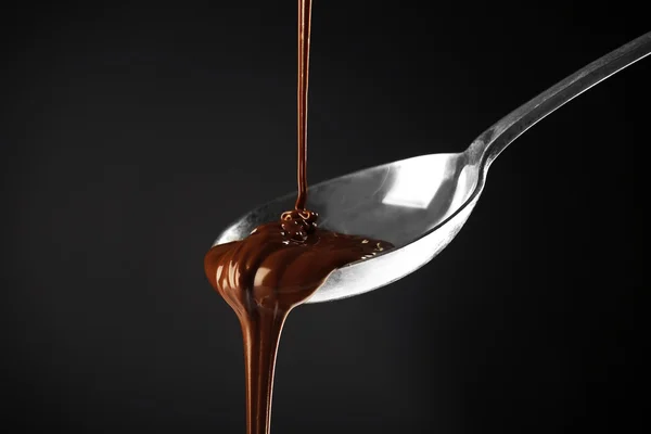 Chocolate derramado em uma colher no fundo escuro — Fotografia de Stock