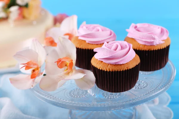 Gustosi cupcake su stand e torta, sul tavolo, sullo sfondo a colori — Foto Stock