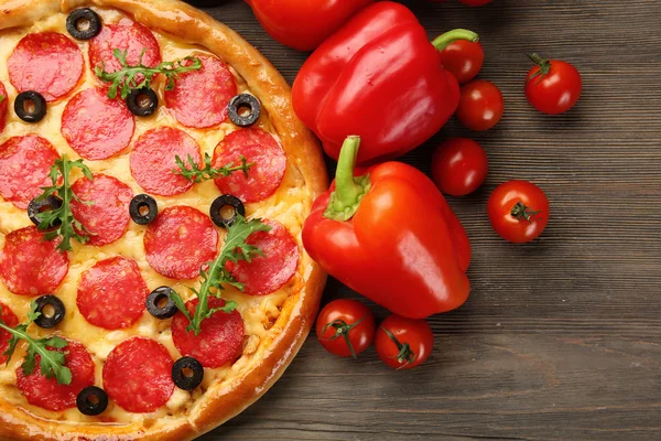살라미와 나무 배경에 빨간색 야채와 맛 있는 피자를 닫습니다. — 스톡 사진