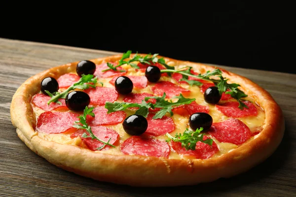 Tasty pizza with salami and olives on wooden table against black background — Stock Photo, Image