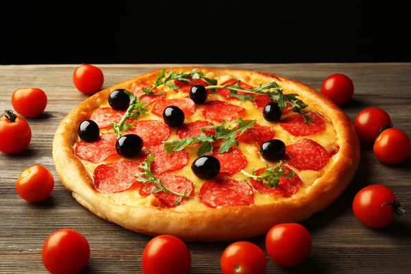 Sabrosa pizza con salami y aceitunas decoradas con tomates sobre mesa de madera sobre fondo negro —  Fotos de Stock