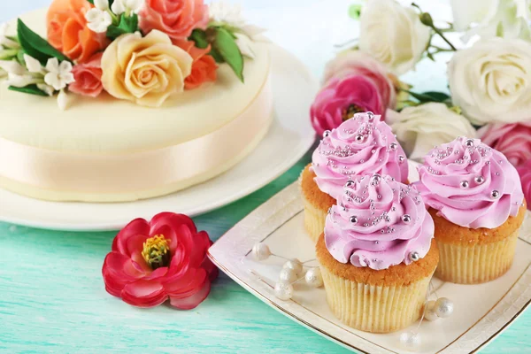 Cake with sugar paste flowers and cupcakes, on light background