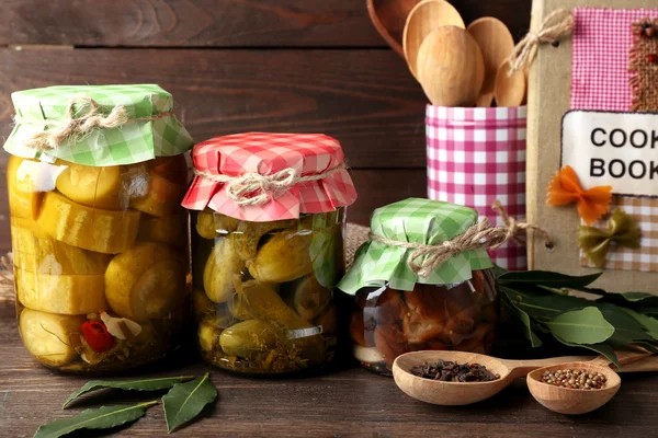 Vasi con verdure sottaceto e fagioli, spezie, libro di ricette e utensili da cucina su sfondo di legno — Foto Stock