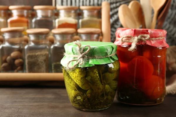 Frascos con verduras y frijoles en vinagre, especias y utensilios de cocina sobre fondo de madera — Foto de Stock