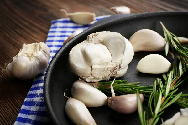 Verse knoflook met rozemarijn in zwarte pan in de buurt van blue Geruit katoen servet op houten achtergrond, close-up — Stockfoto