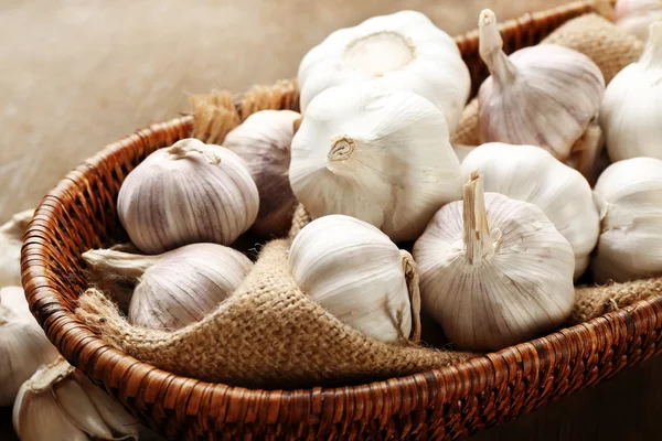 Garlic in wicker bowl on wooden background, close up — Stock Photo, Image