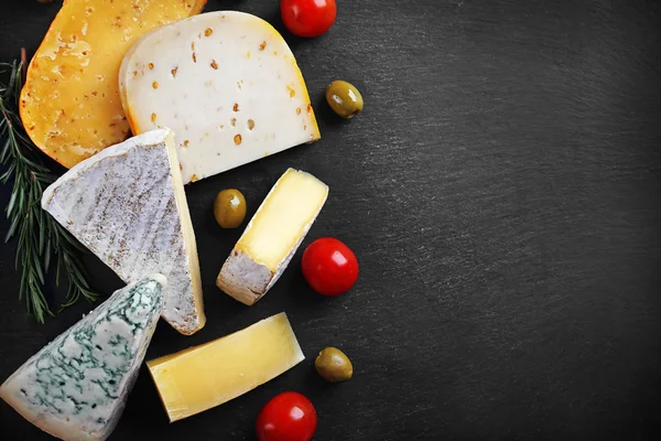 Diferentes tipos de queso, tomates y aceitunas en pizarra negra, espacio para copiar — Foto de Stock