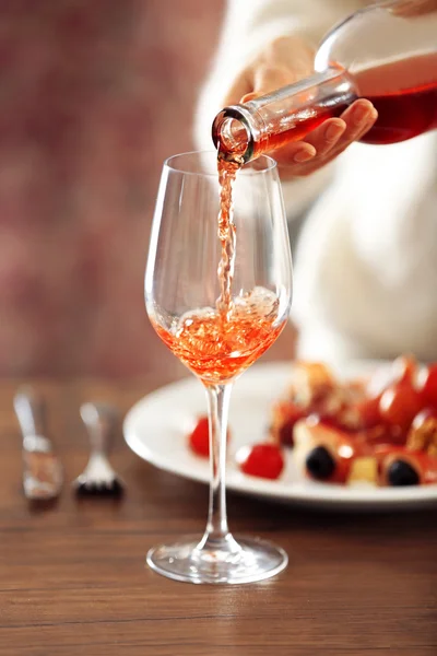 Mujer joven vertiendo vino rosa en el vaso sobre la mesa — Foto de Stock