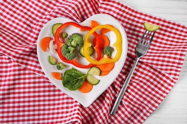 Useful cut vegetables on a plate in the form of heart on wooden table top view — Stock Photo, Image