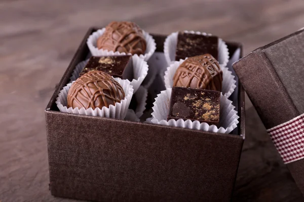 在精美的礼品盒，木制背景上的美味巧克力糖果 — 图库照片