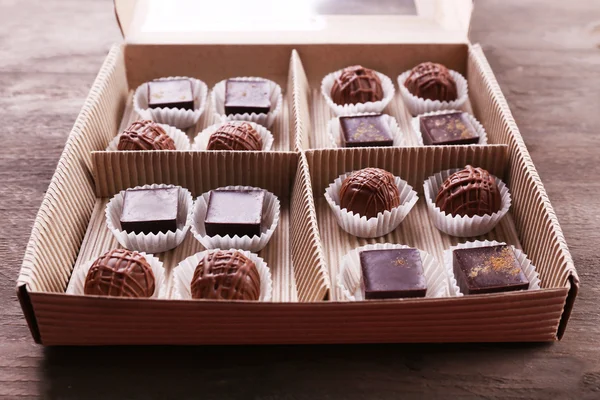 Heerlijke chocolade snoepjes in papier vak op houten achtergrond, close-up — Stockfoto