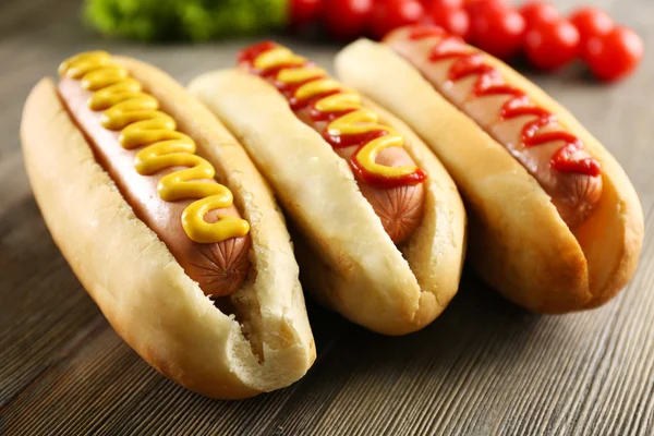 Cachorros-quentes saborosos com legumes no fundo de madeira — Fotografia de Stock