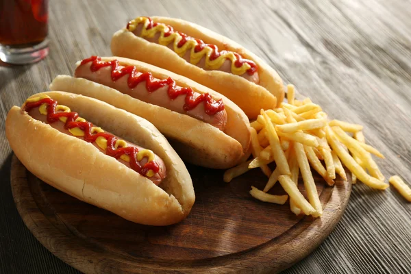 Deliciosos perritos calientes con papas fritas sobre tabla de cortar de madera, de cerca — Foto de Stock