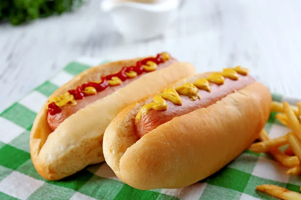 Deliciosos perritos calientes con papas fritas en servilleta de algodón a cuadros verde, de cerca — Foto de Stock