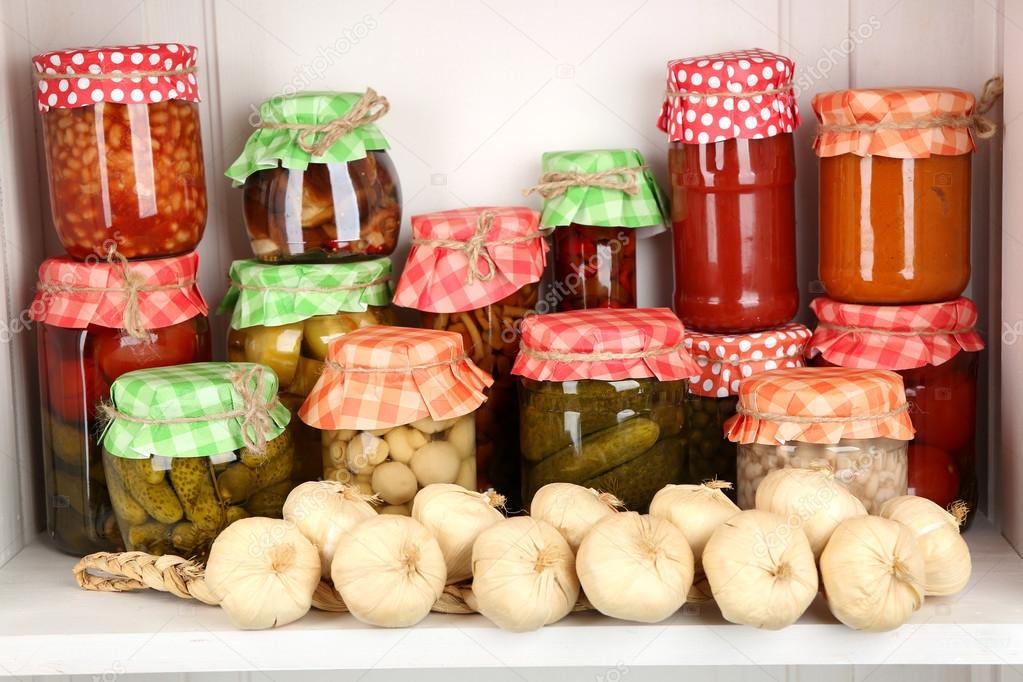 Jars with pickled vegetables and beans on wooden shelf