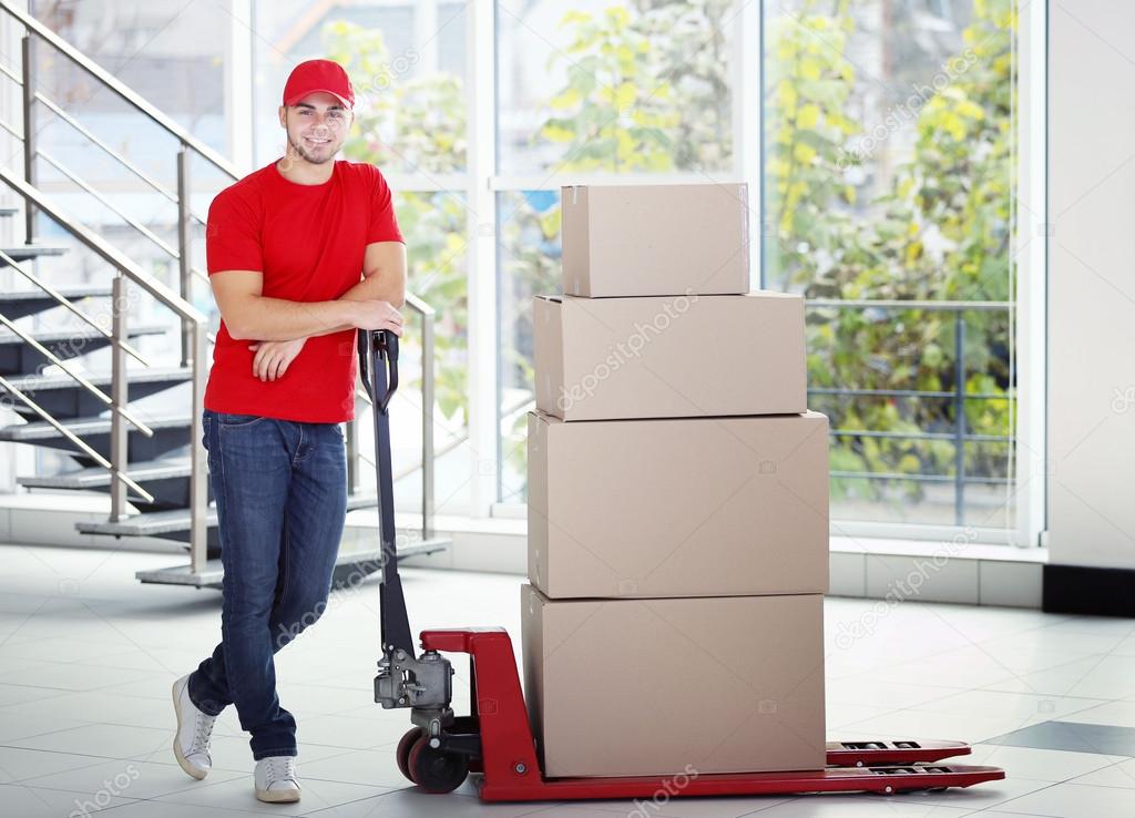 Postman in red uniform with parcels on dolly