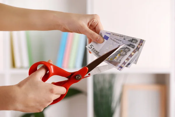 Hands with scissors cutting Euro banknotes, on blurred interior background — Stock Photo, Image