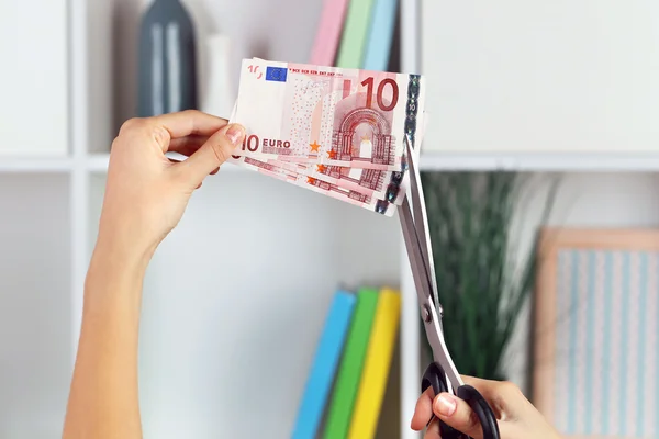 Hands with scissors cutting Euro banknotes, on blurred interior background — Stock Photo, Image