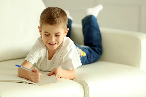 Menino escrevendo em caderno em um sofá — Fotografia de Stock