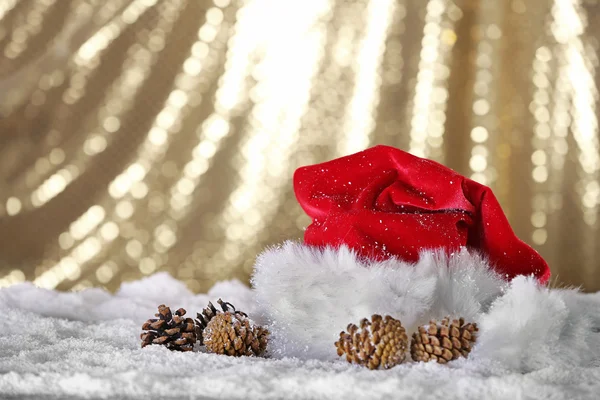 Santa Claus červená čepice s šišky na umělý sníh na pozadí zlatých zblízka — Stock fotografie