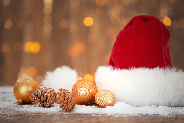 Santa Claus czerwony kapelusz z ozdób świątecznych na sztucznym śniegu z błyszczącym tle, z bliska — Zdjęcie stockowe