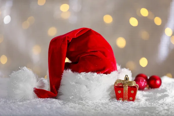 Sombrero rojo de Santa Claus con decoraciones navideñas en la nieve artificial sobre fondo brillante, primer plano —  Fotos de Stock