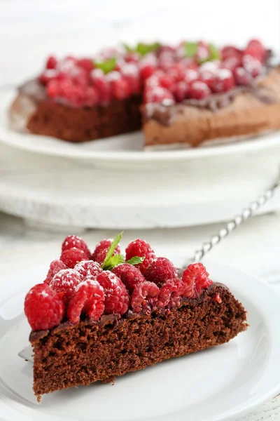Stück Kuchen mit Schokoladenglasur und Himbeeren auf farbigem Holzhintergrund — Stockfoto