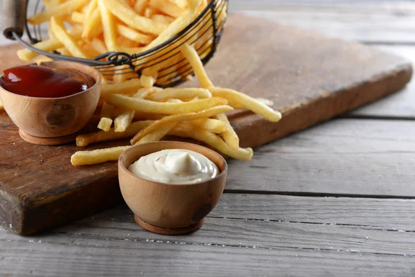 Γαλλικά τηγανίζονται πατάτες σε μεταλλικό καλάθι σε ξύλινα φόντο — Φωτογραφία Αρχείου