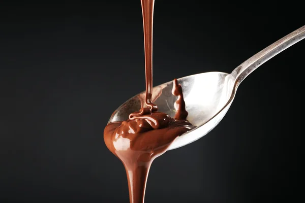 Suklaa kaadetaan lusikalla tummalla pohjalla — kuvapankkivalokuva
