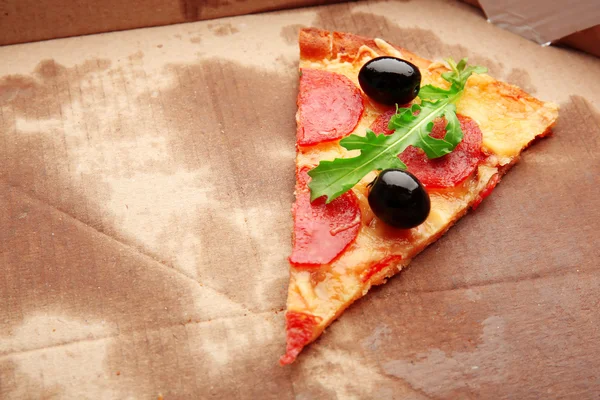 Plak van pepperoni pizza met rucola en olijven op karton — Stockfoto