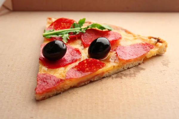 Plak van pepperoni pizza met rucola en olijven op karton — Stockfoto