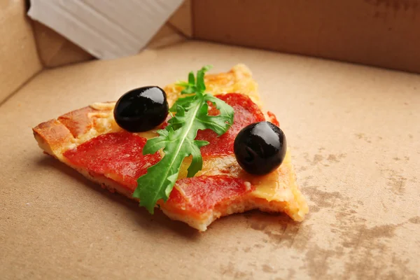 Ugryziony kawałek pepperoni pizza z oliwkami i rukolą na tekturze — Zdjęcie stockowe