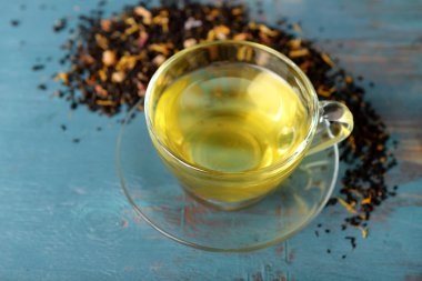 Cam bardak çay yeşil yaprakları ile ve mavi ahşap arka plan etrafında dağınık çay