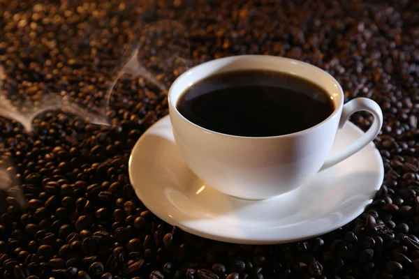 Cup med varmt kaffe på kaffebönor bakgrund — Stockfoto
