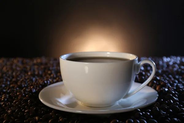 Kop varm kaffe blandt kaffebønner på mørk baggrund - Stock-foto