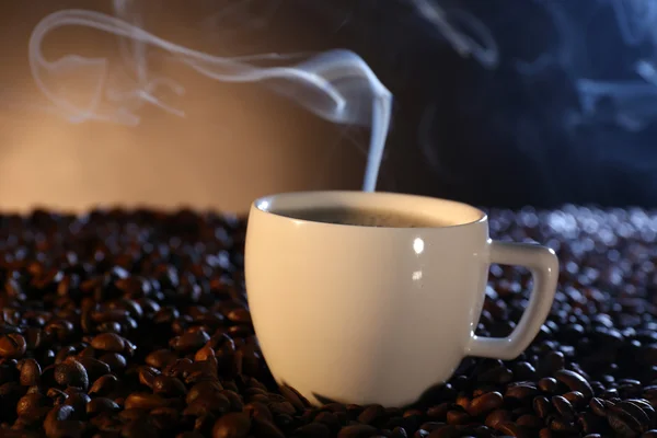 Kopp varm kaffe bland kaffebönor på mörk bakgrund — Stockfoto