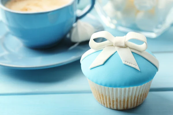 Leckerer Cupcake mit Schleife, Kaffeetasse und Weihnachtsspielzeug auf farbigem Holzhintergrund — Stockfoto