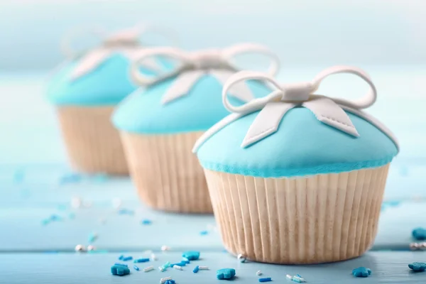 Cupcakes saborosos com arco na cor de fundo de madeira — Fotografia de Stock